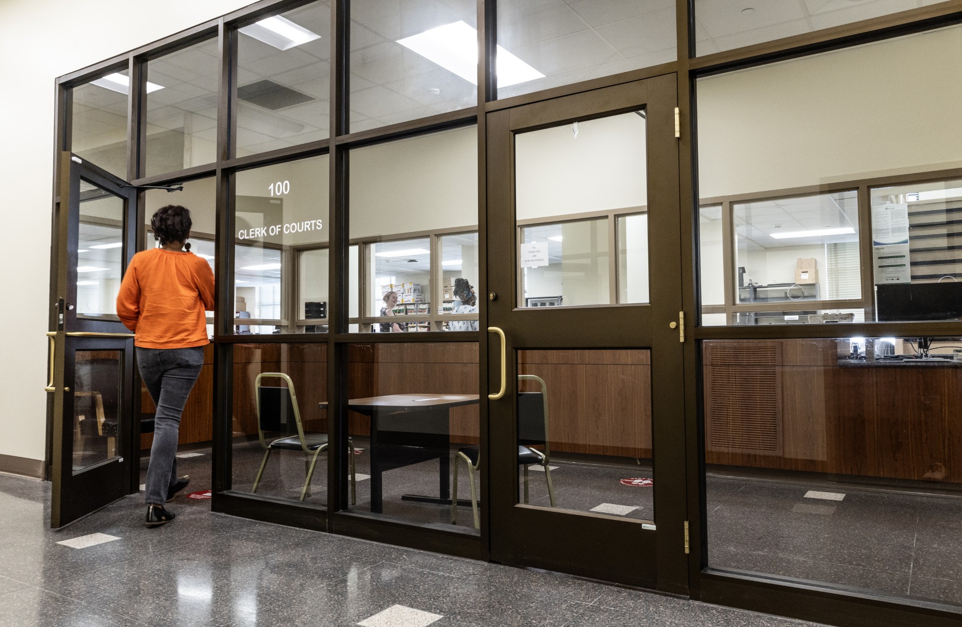 A clerk behind a glass window hands a stack of printed court records to a member of the public in a courthouse lobby