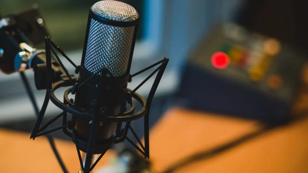 A condenser microphone beside a laptop showing an audio editing timeline in a home office