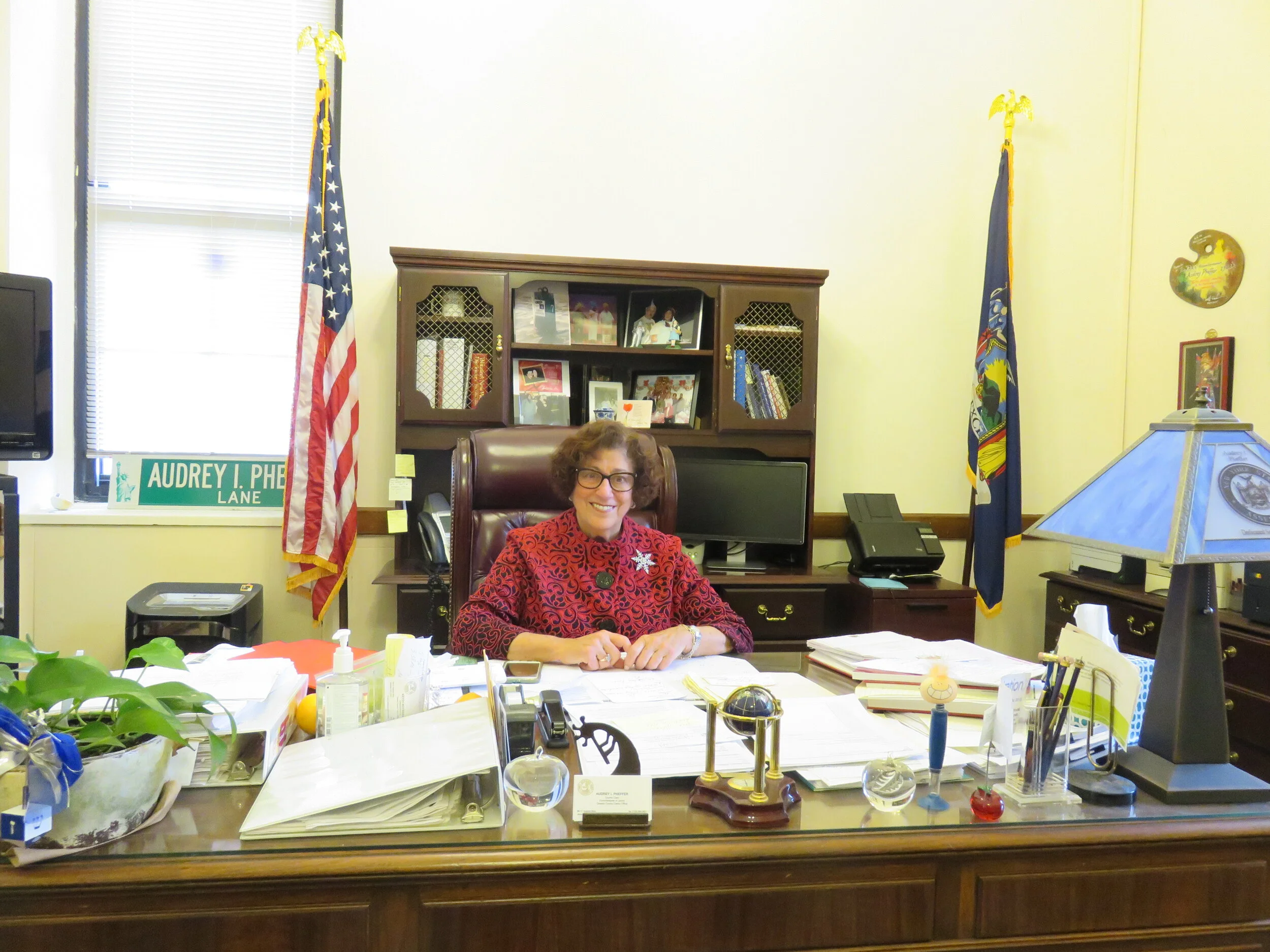 A county records office clerk seated at a desk with file boxes and a computer, captured in a candid office environment
