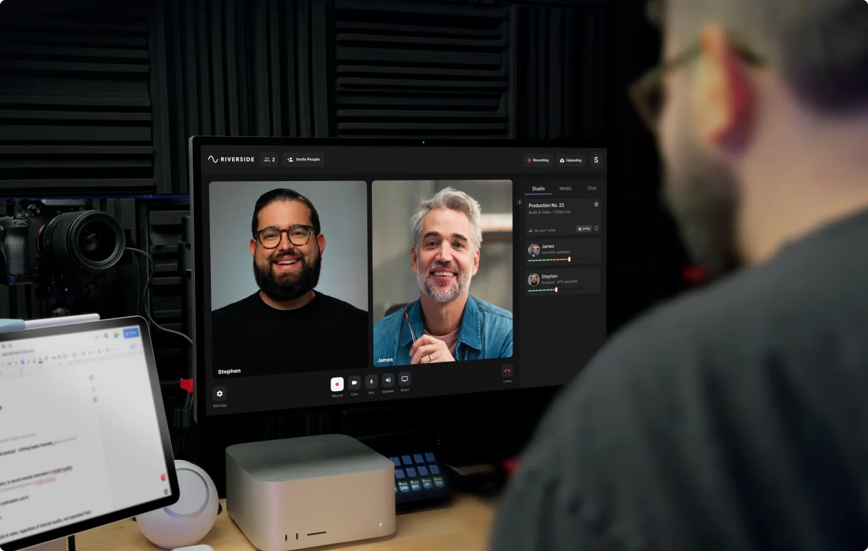 A laptop on a desk showing a video call while an external microphone and headphones are set up for a remote podcast interview