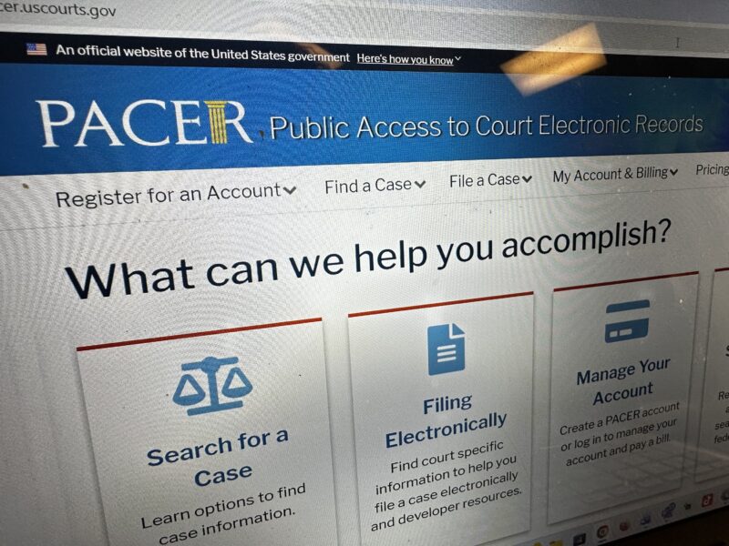 A laptop screen showing a federal court docket interface with case entries listed, photographed over a desk with a notebook and pen beside it