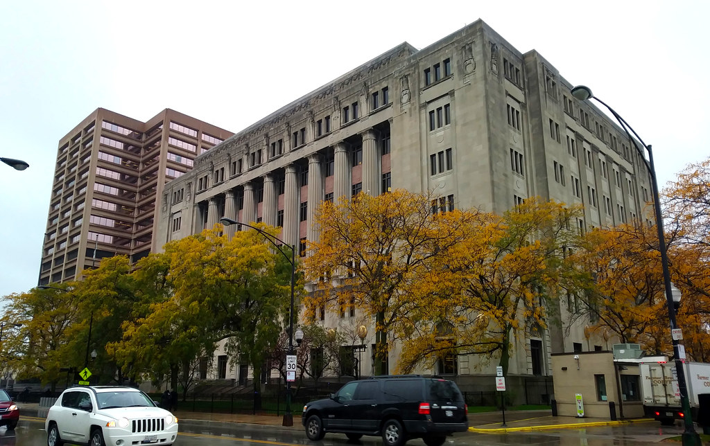 A large urban criminal courthouse building with people entering through security checkpoints on a weekday morning