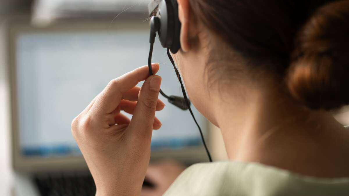 A person seated at a desk with a computer and headset in an office setting, suggesting a support hotline call center