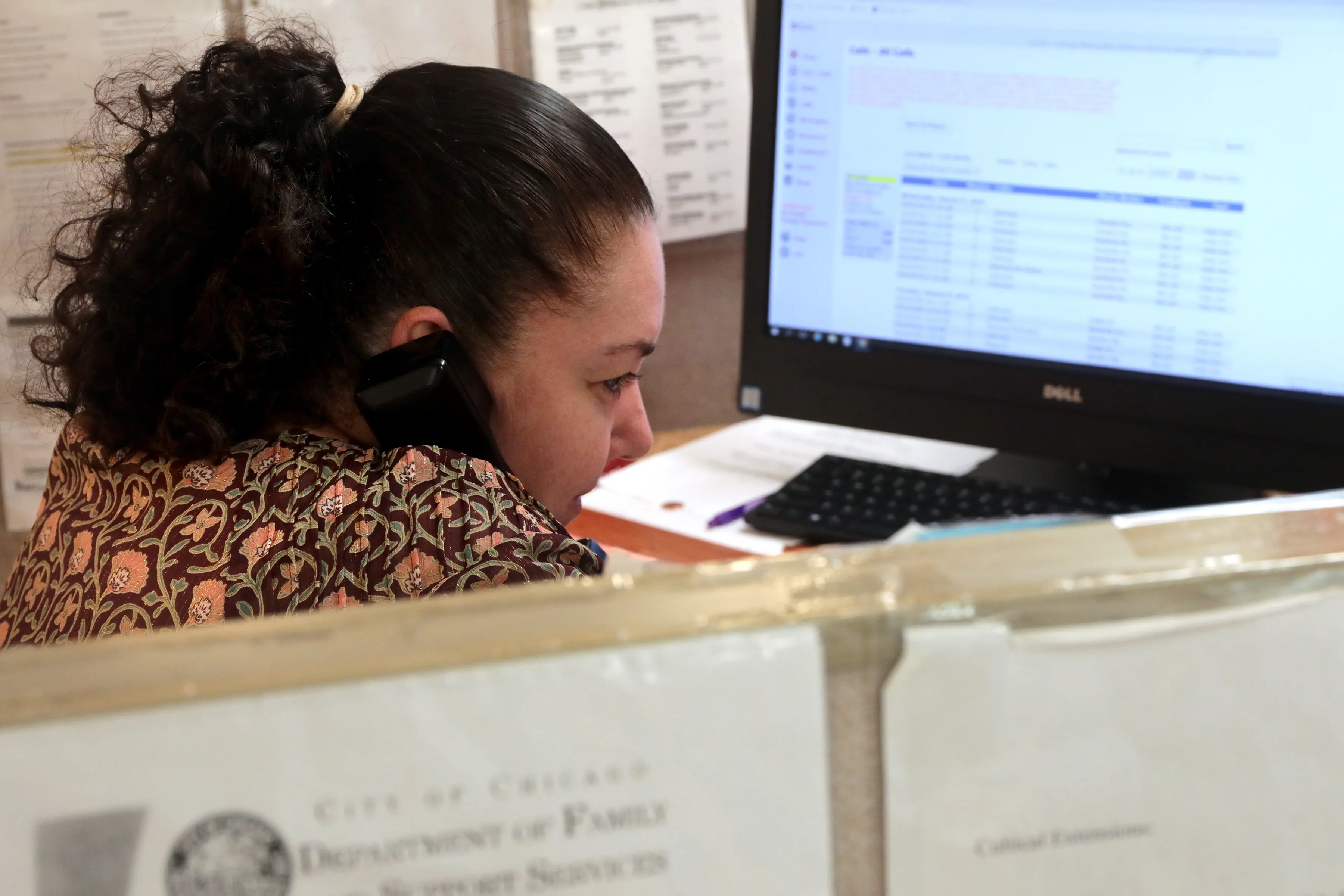 A person sitting at a kitchen table holding a phone, shoulders tense, suggesting the stress of making a report and not being believed