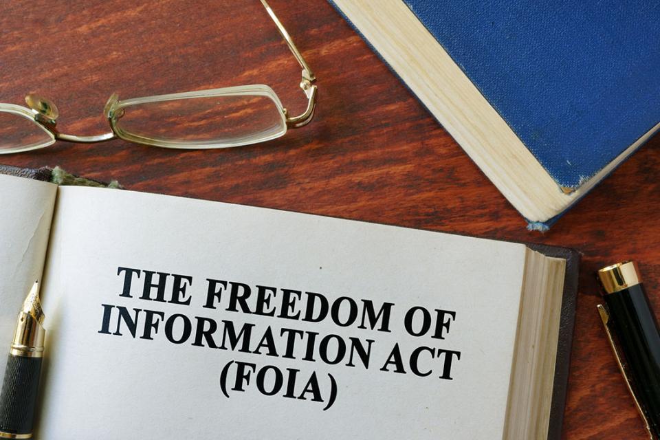 A person’s hands sorting printed public records request paperwork beside a laptop showing an email thread with a government records office