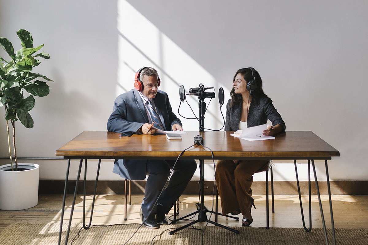 A podcast microphone on a desk next to a laptop and printed notes in a small recording space