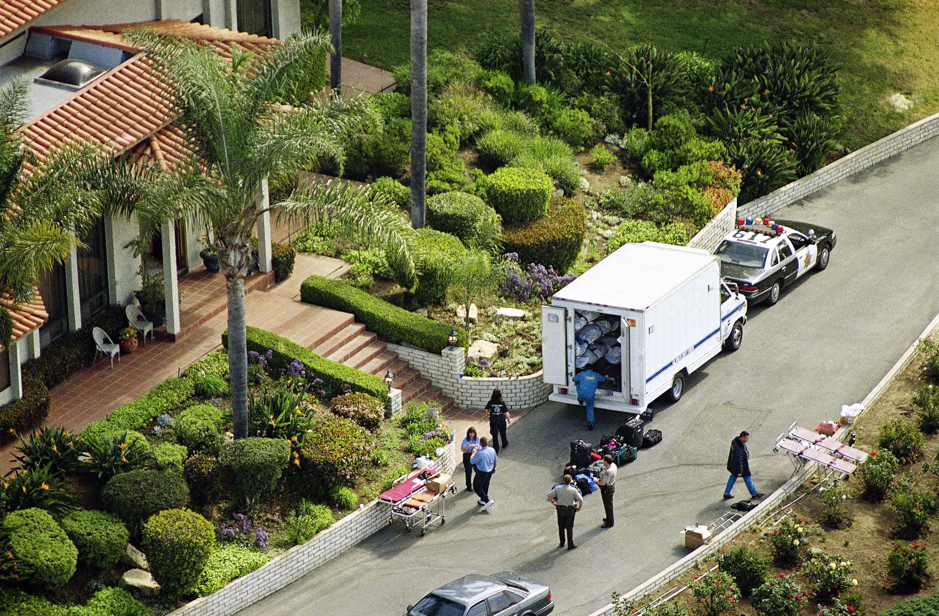 A quiet residential street in Rancho Santa Fe, California, with police vehicles and officers gathered outside a home connected to the Heaven's Gate case