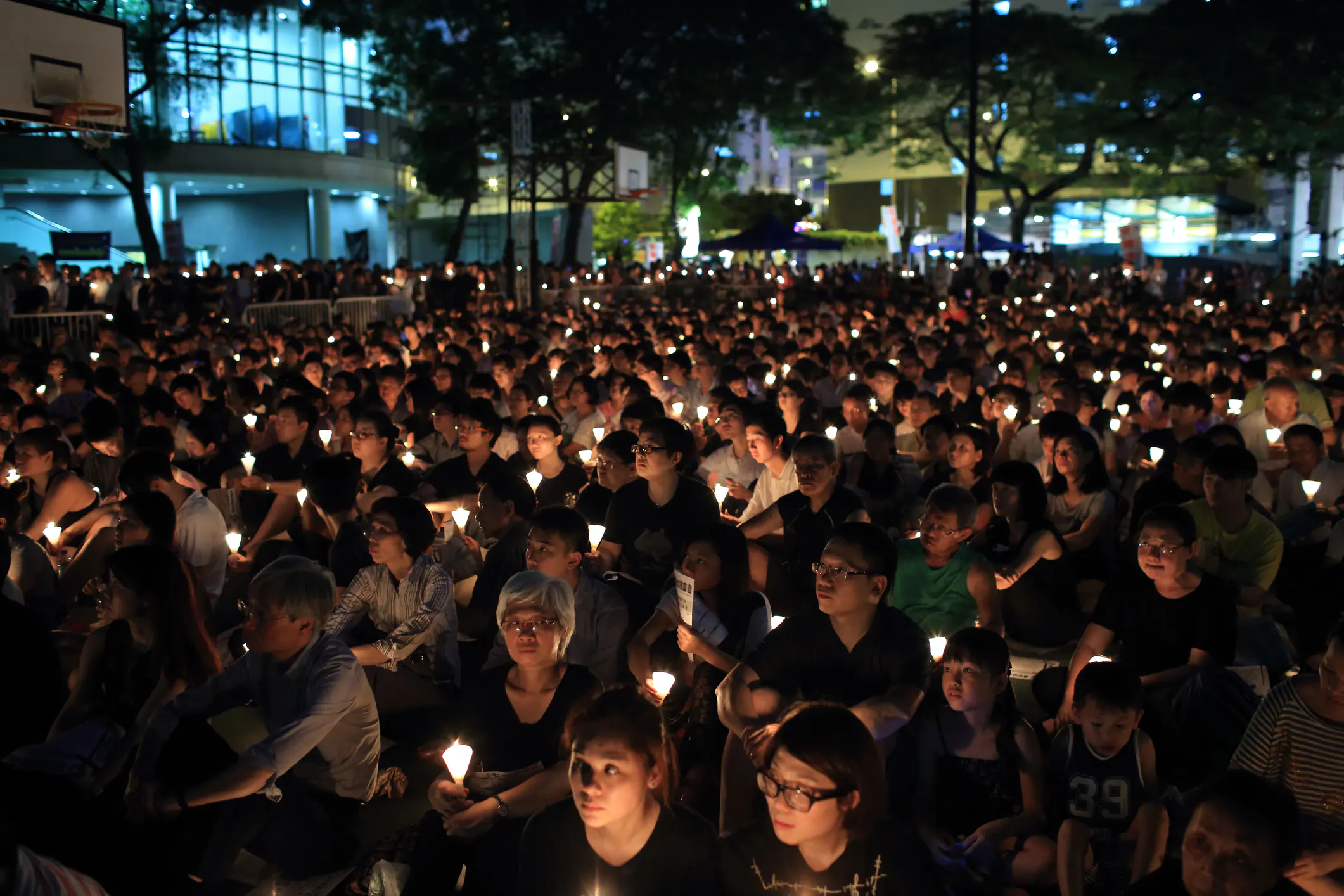 A small evening vigil with candles and flowers arranged on a sidewalk near a framed photograph, capturing a quiet community memorial
