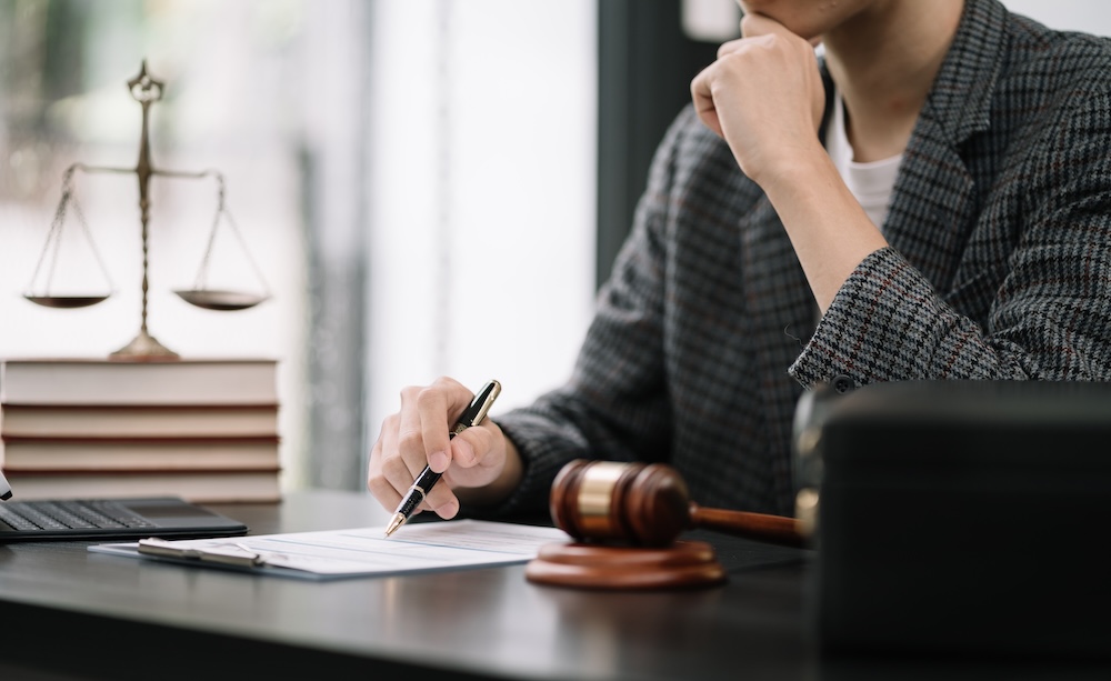A stack of printed court documents and a manila case file folder on a wooden table, with a pen resting on top