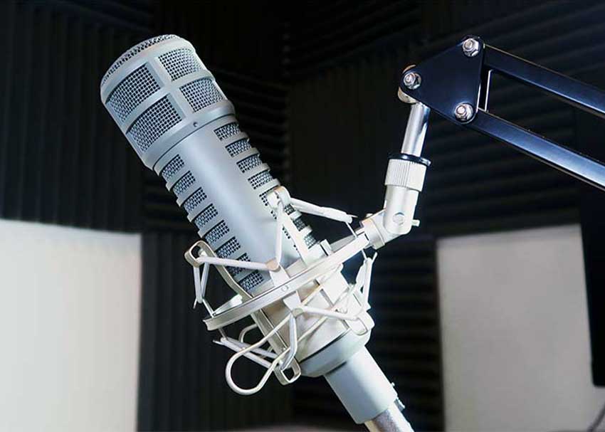 A studio microphone on a boom arm across from a chair with a notepad on the seat