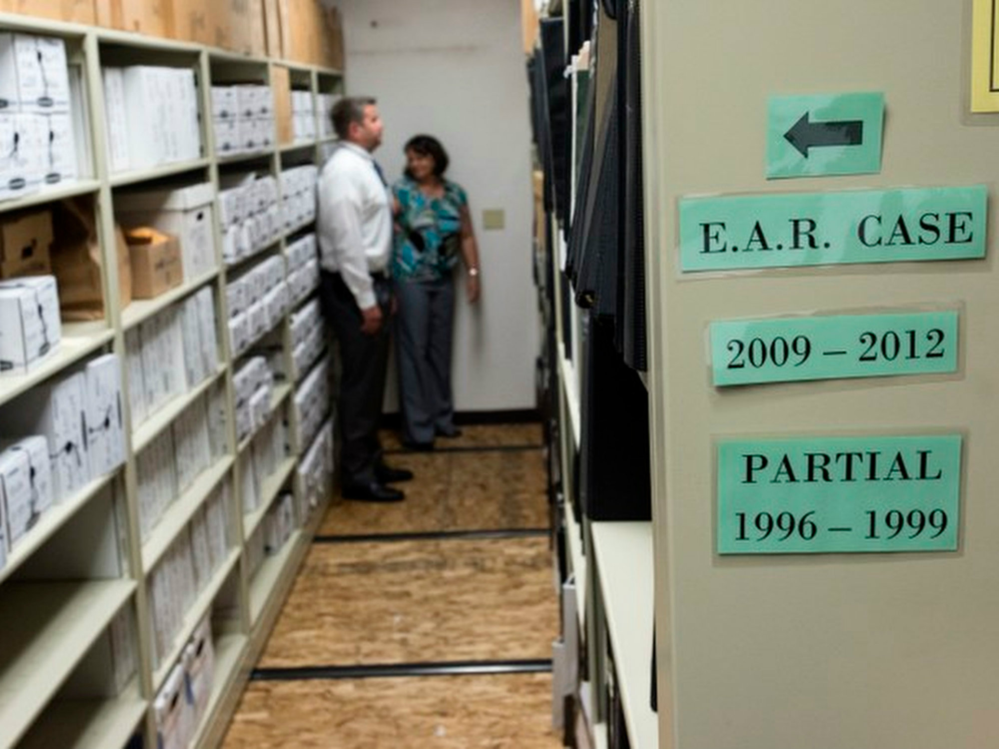 A tabletop arrangement of case materials including printed reports and archival photographs, suggesting a long-running investigation and the accumulation of evidence over time