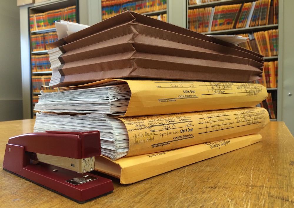 A thick case file folder on a desk with tabs and paper documents partially visible under warm desk lighting