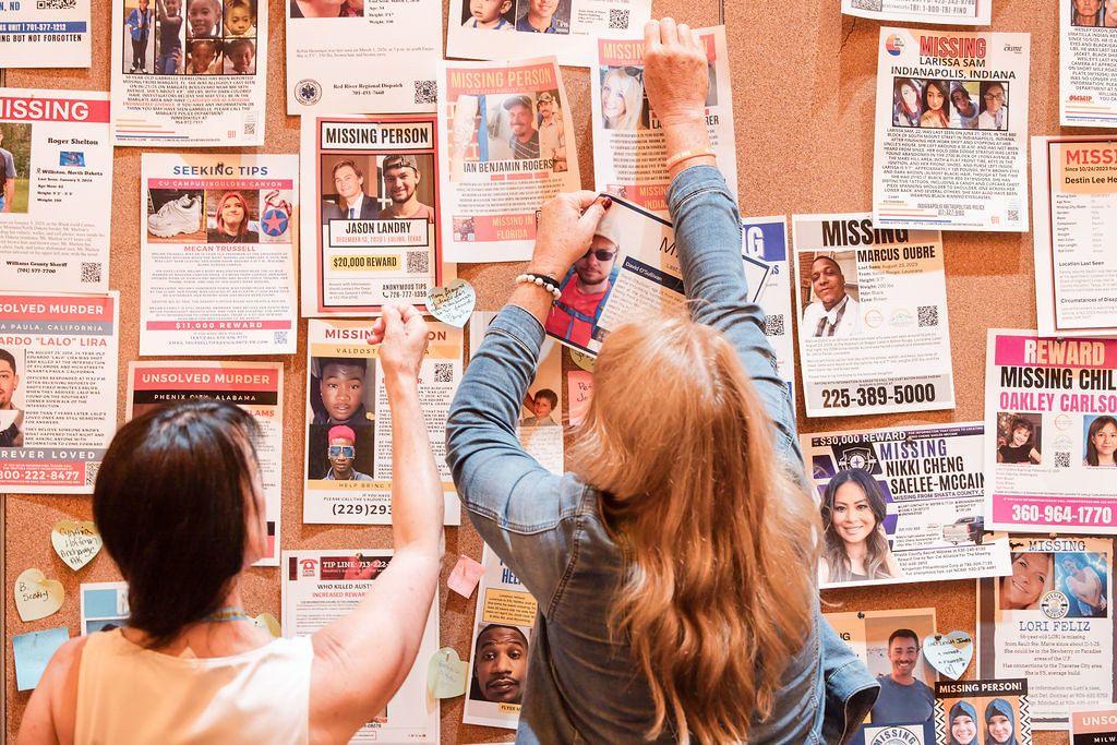 A volunteer standing behind a folding table covered with brochures and donation materials at a community fundraiser event inside a local hall