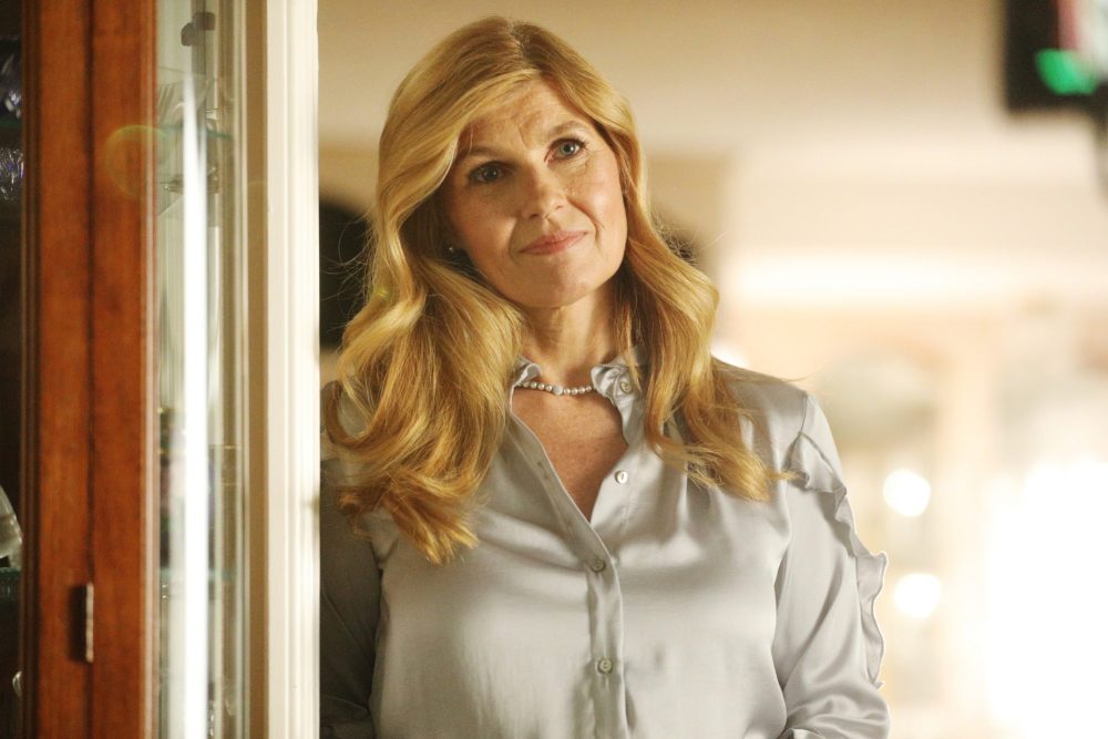 Actor Connie Britton in a warmly lit kitchen holding a phone and looking worried in a television drama still