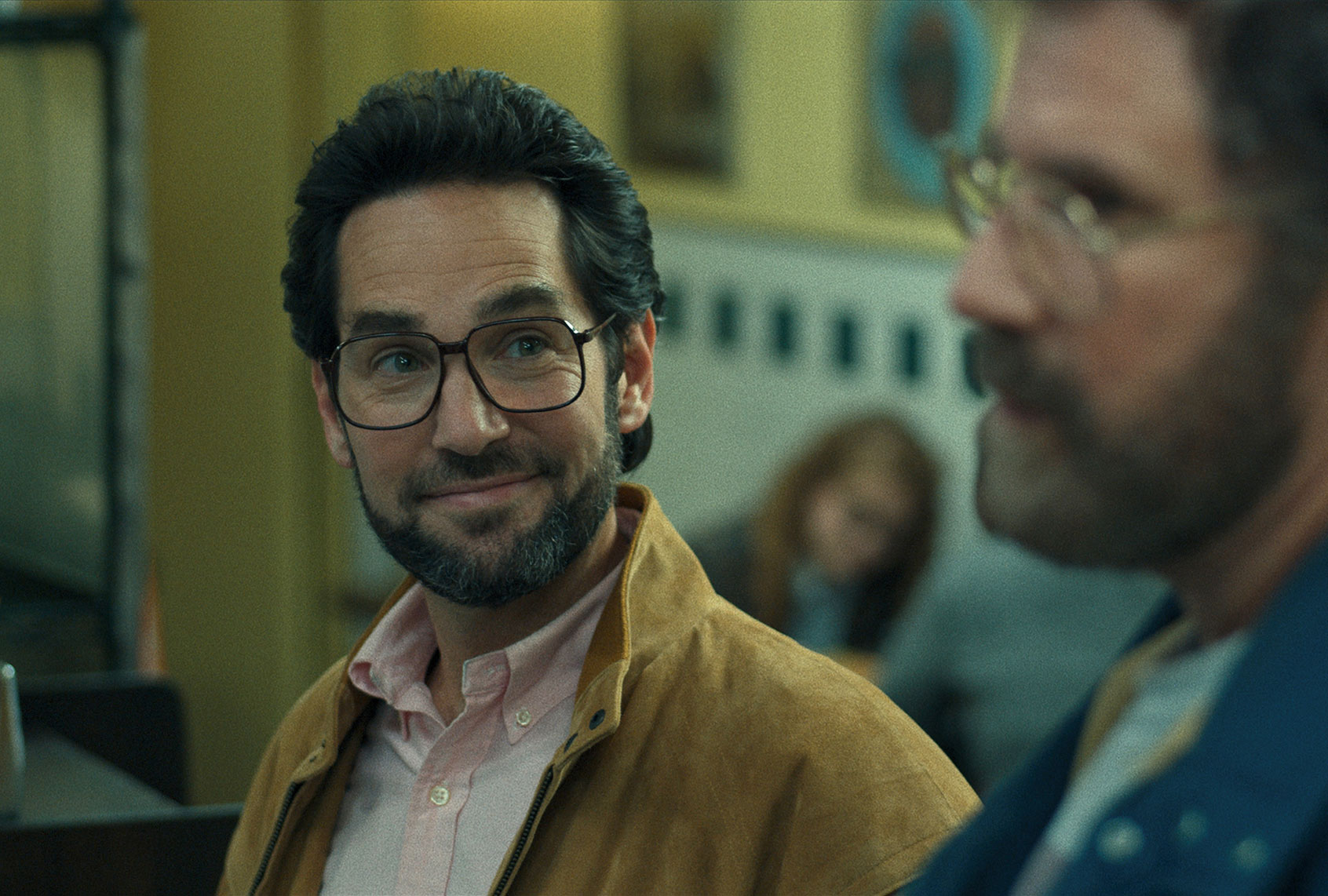 Actor Paul Rudd in glasses and a suit seated in a therapist office with a calm expression in a television drama still