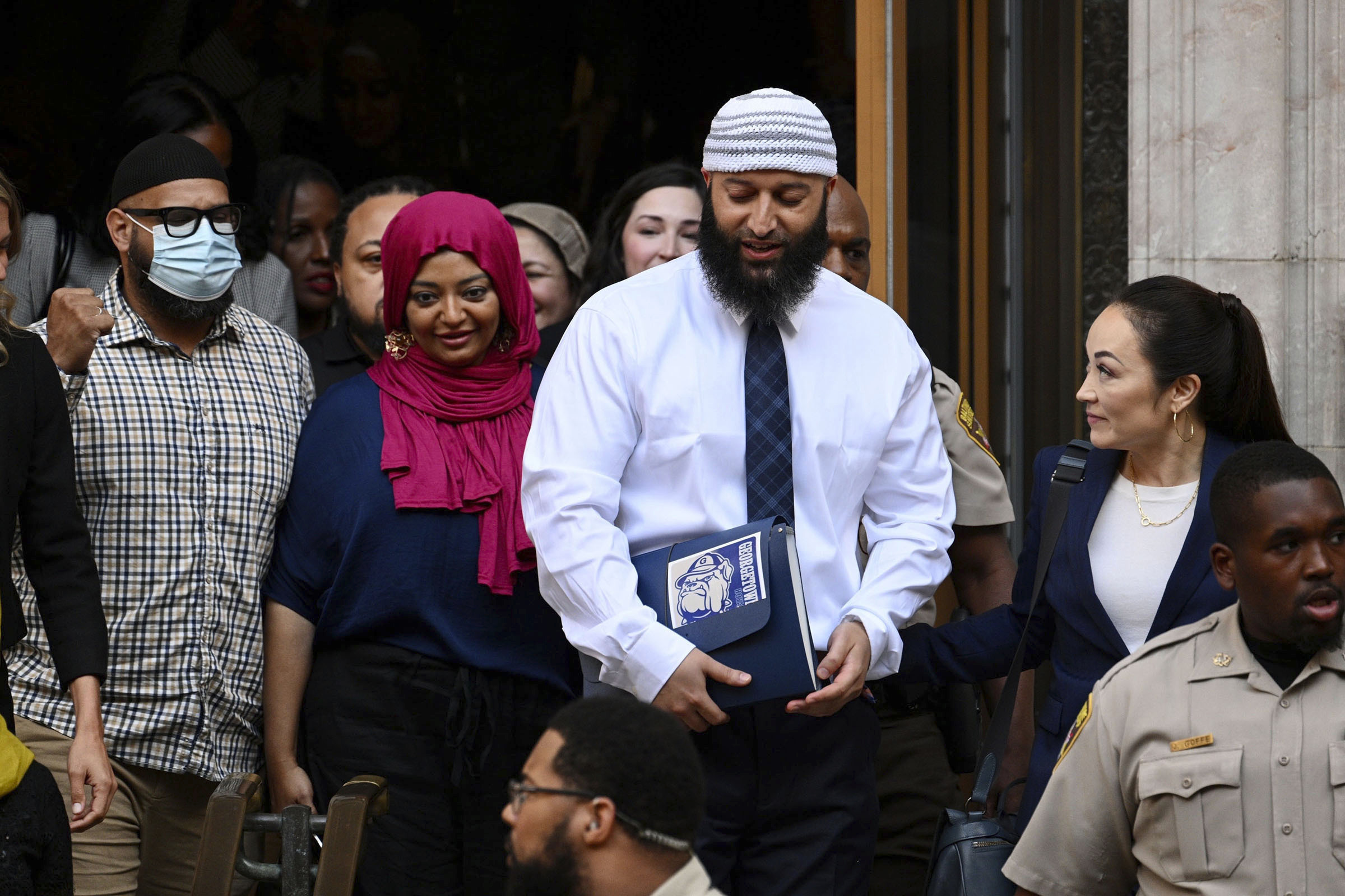 Adnan Syed arriving at a courthouse with attorneys and reporters gathered nearby
