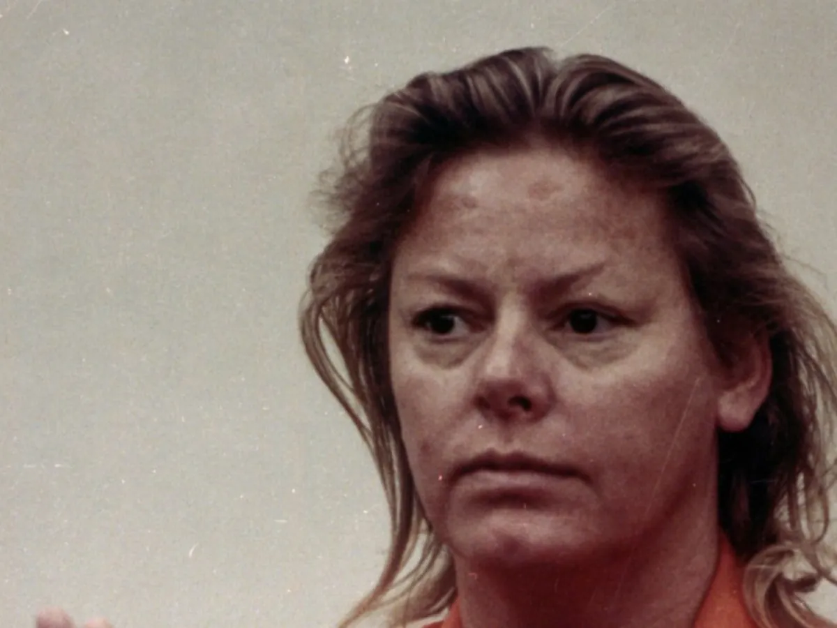 Aileen Wuornos faces the camera in a jail booking portrait under harsh overhead lighting against a plain background