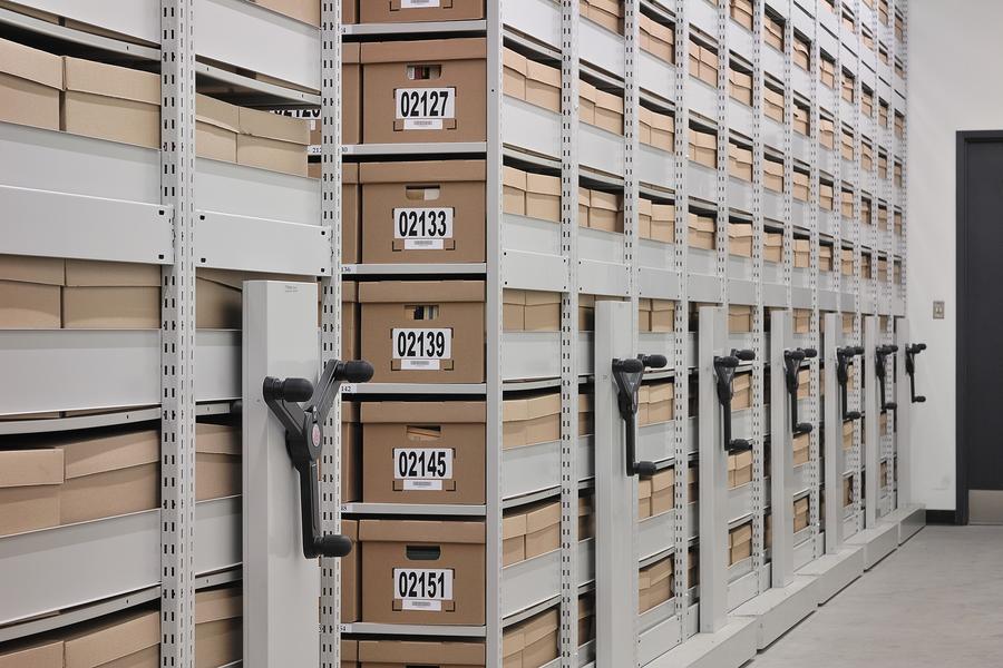 Cardboard evidence boxes stacked on metal shelving in a police records room, sealed and labeled with case numbers
