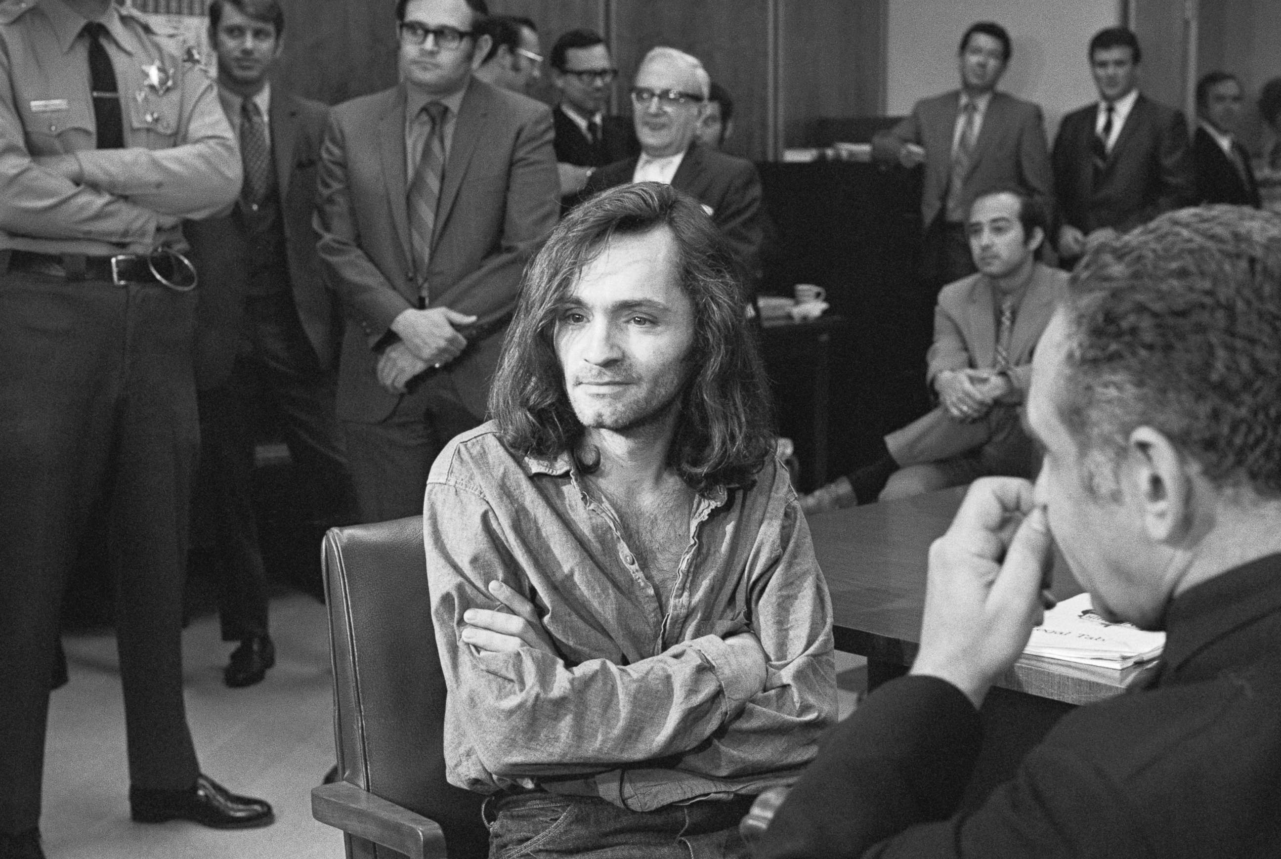 Charles Manson seated in a courtroom during his 1970 trial, surrounded by attorneys and court personnel, news photography style