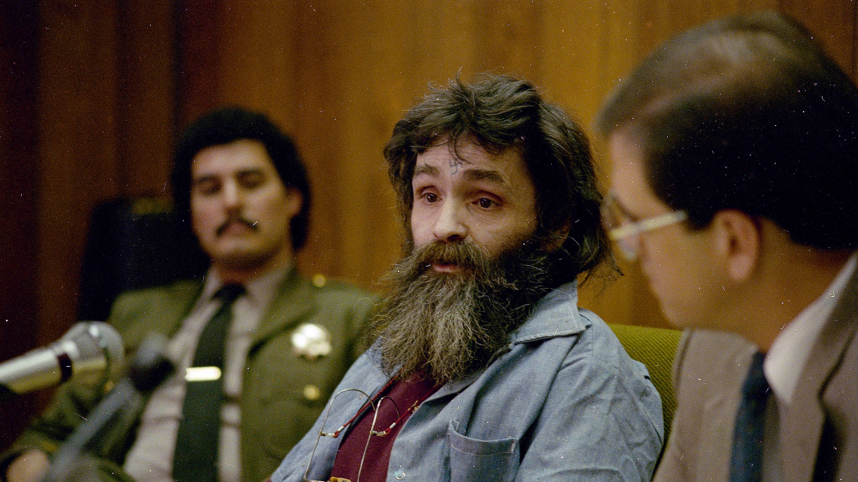 Charles Manson seated in a courtroom during his early 1970s trial, surrounded by legal personnel