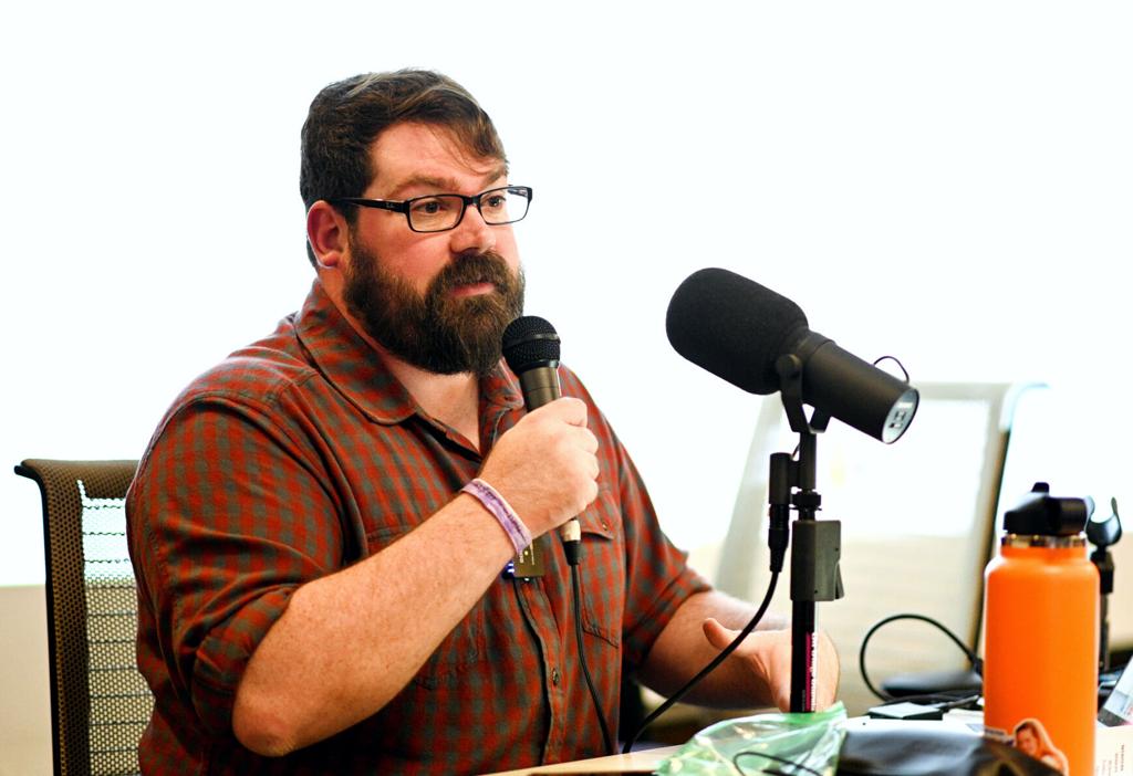 Chris Lambert seated at a desk with a laptop and audio recorder, reviewing printed case notes in a quiet home office