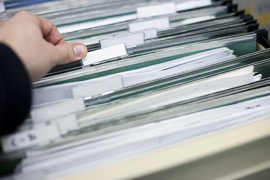Printed court documents and a highlighted timeline spread across a desk next to an open notebook and a cup of tea